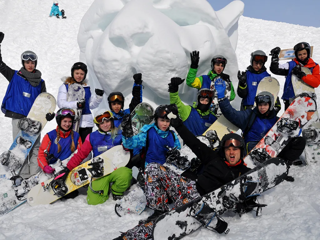 Gruppe posiert mit Snowboards vor einer Schneeskulptur.